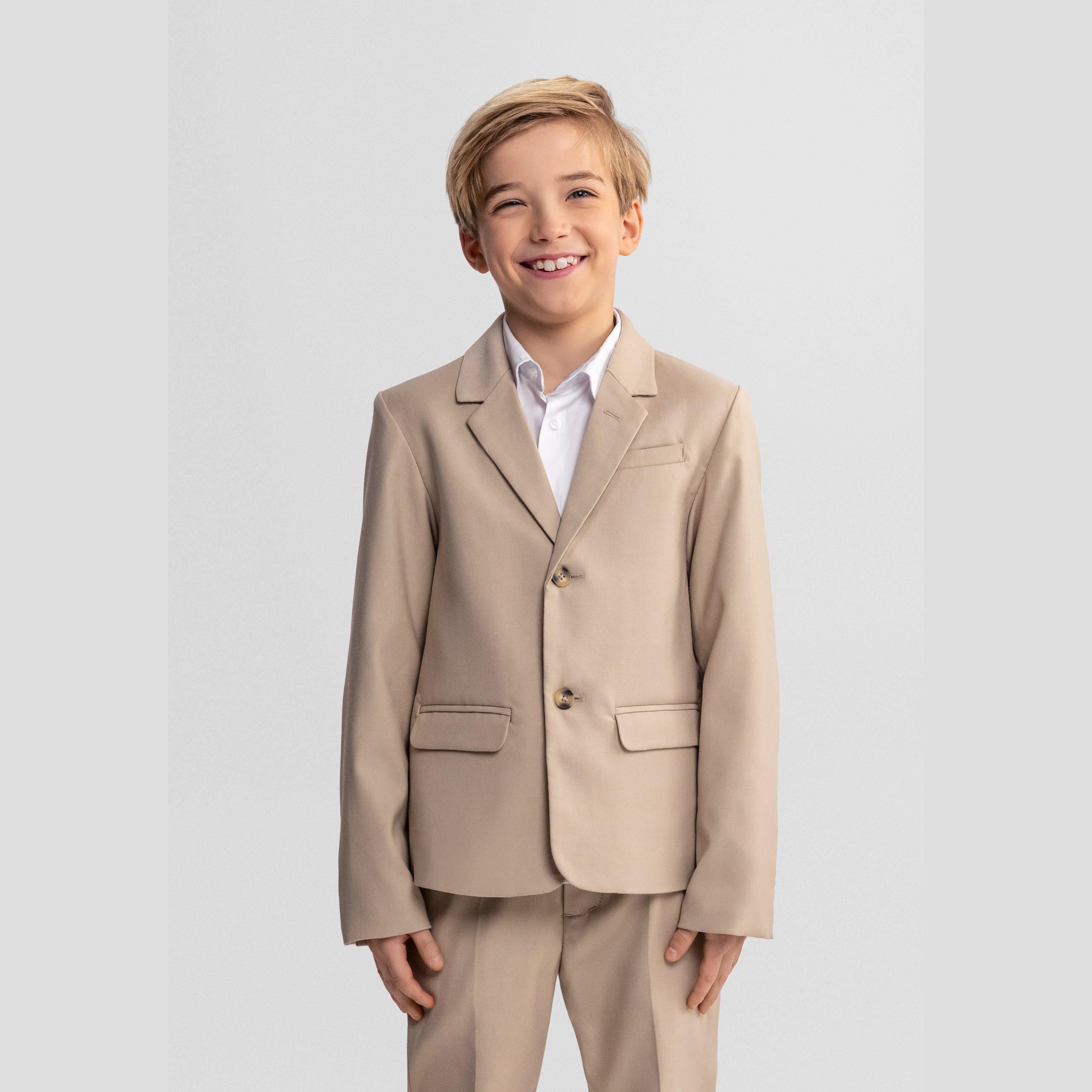 Young blonde boy wearing stone coloured formal blazer with white shirt, smiling at camera against light grey background