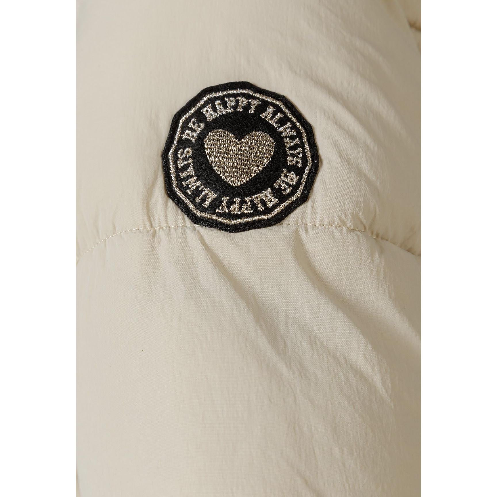 Close-up detail of circular embroidered patch with heart design and text on beige quilted puffer jacket fabric