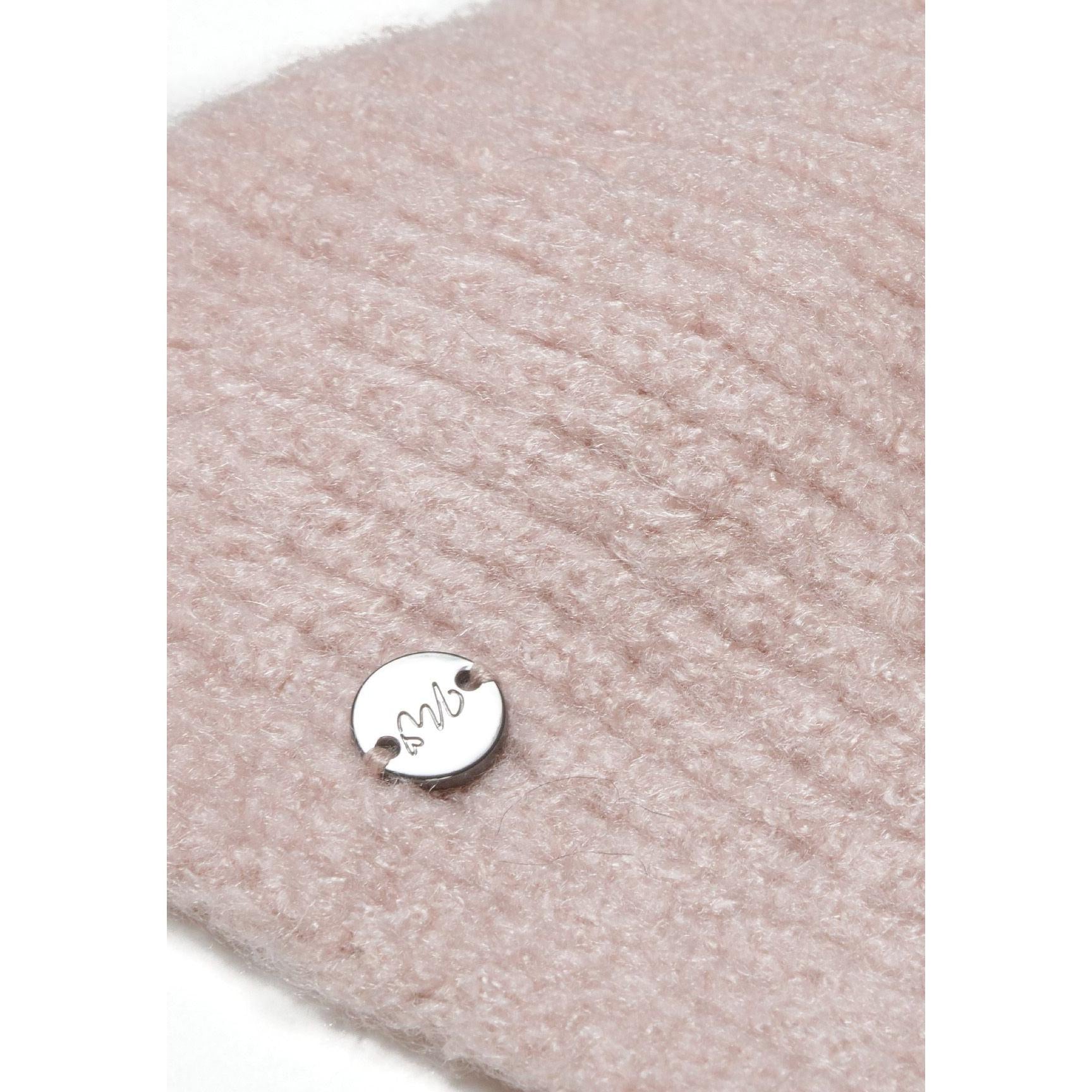 Close-up detail of pale pink ribbed knit fabric texture showing round metal Minoti brand badge