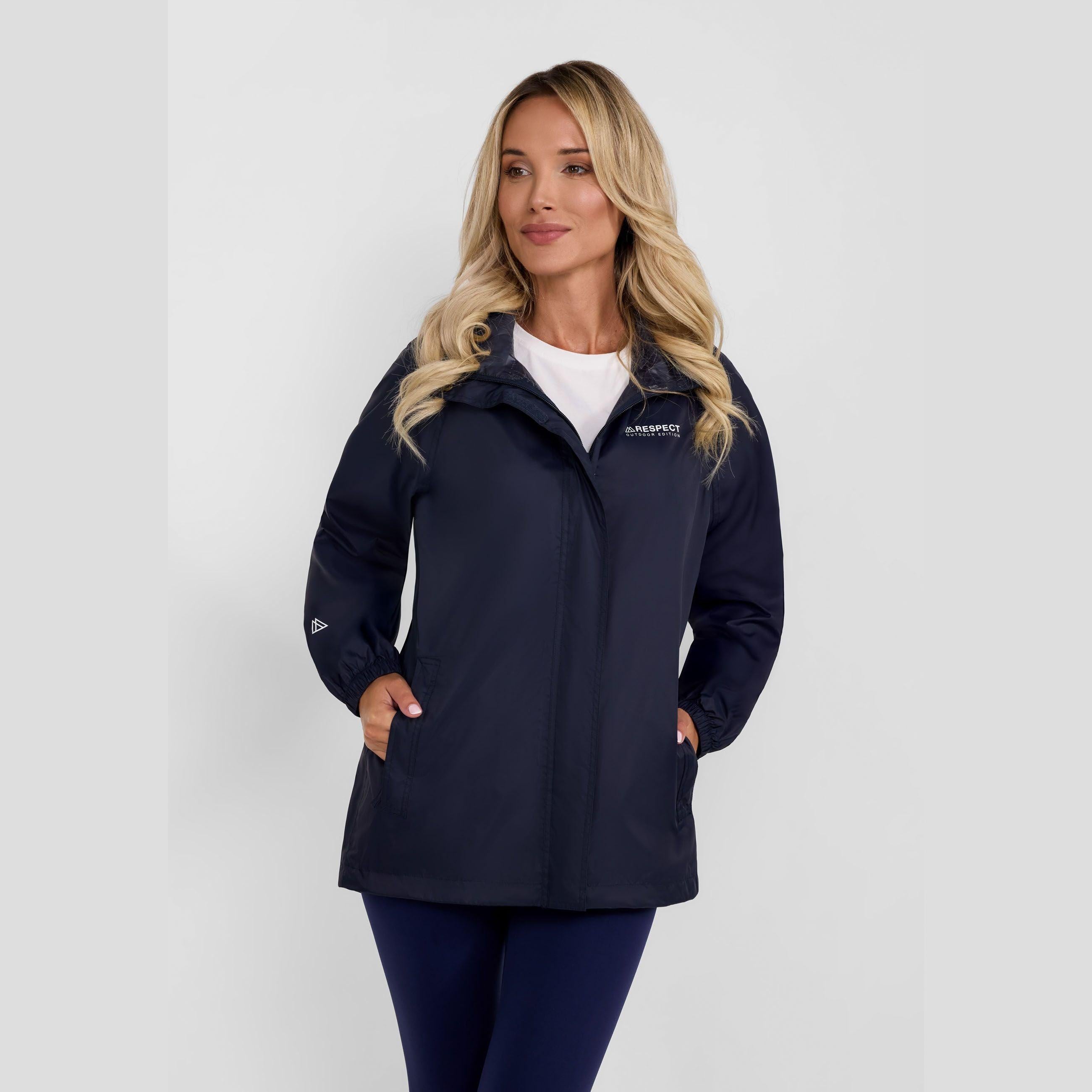 Woman wearing navy packaway waterproof jacket with concealed hood, standing against white background, paired with blue jeans