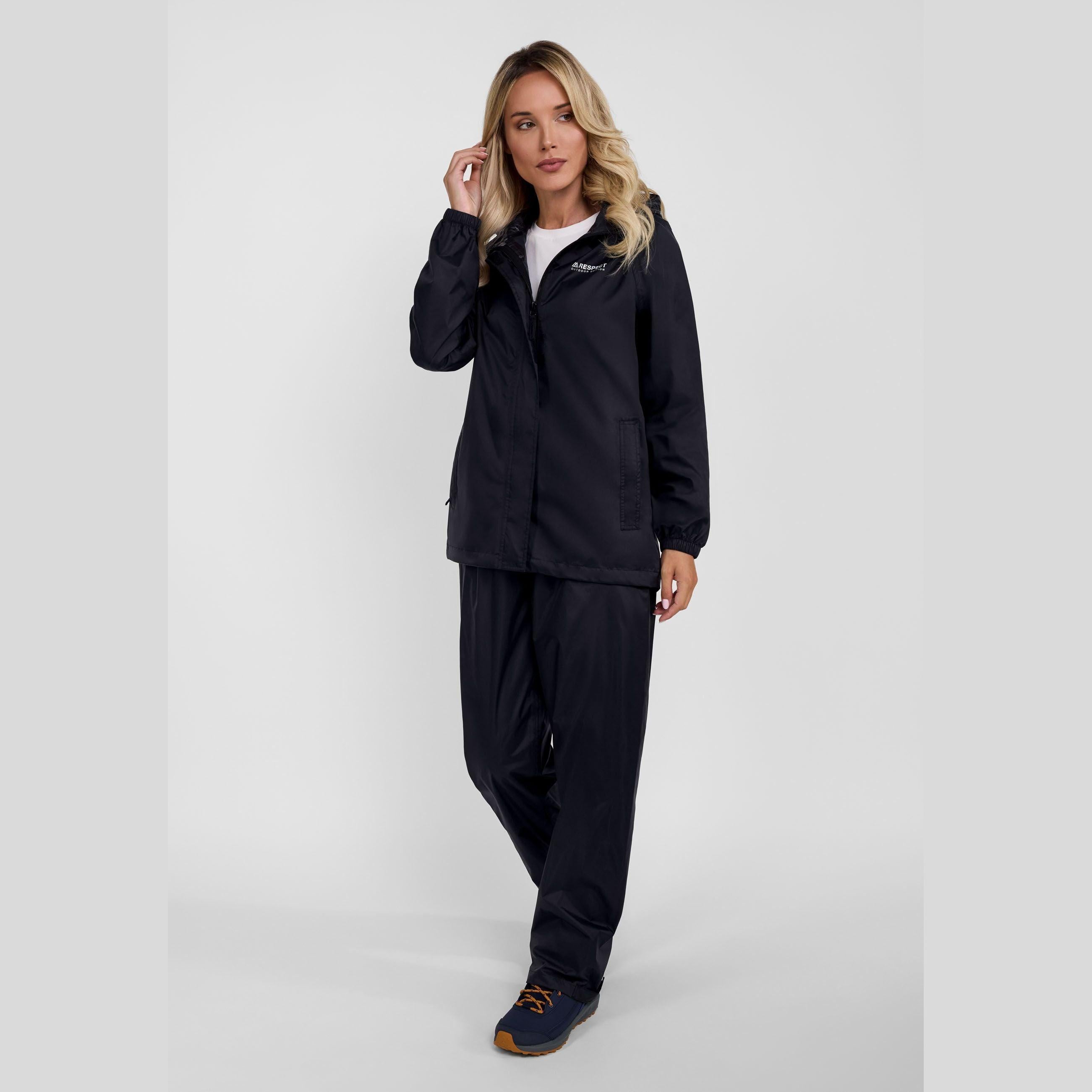 Woman wearing black waterproof overpants and jacket outfit standing against white background