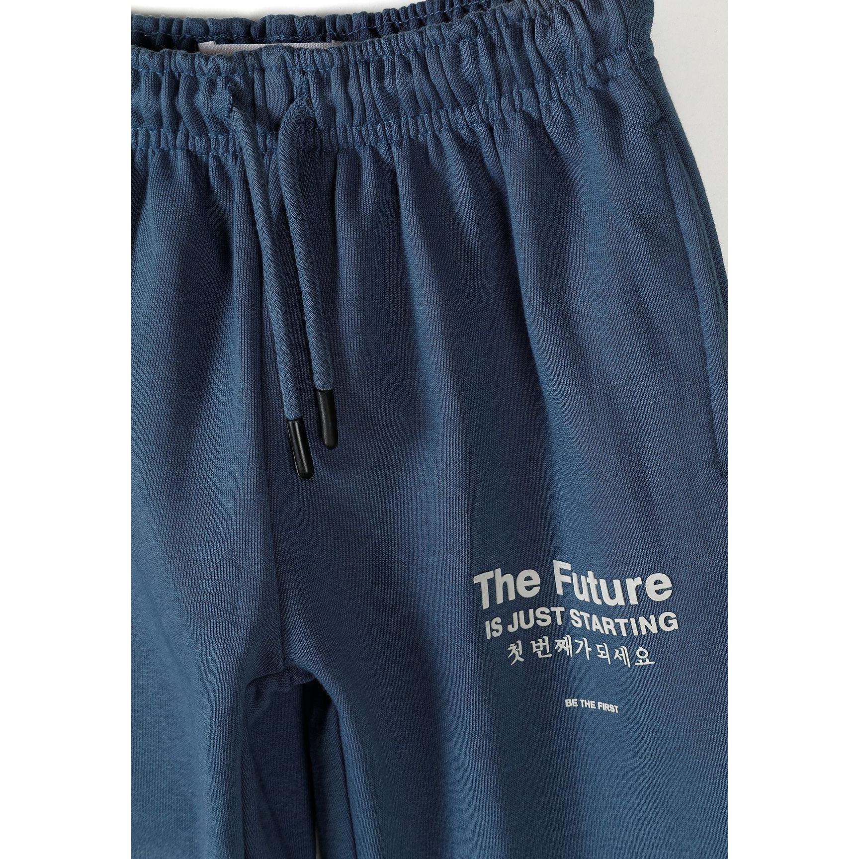 Close-up of blue joggers waistband showing elasticated waist with drawstring and matching text graphics