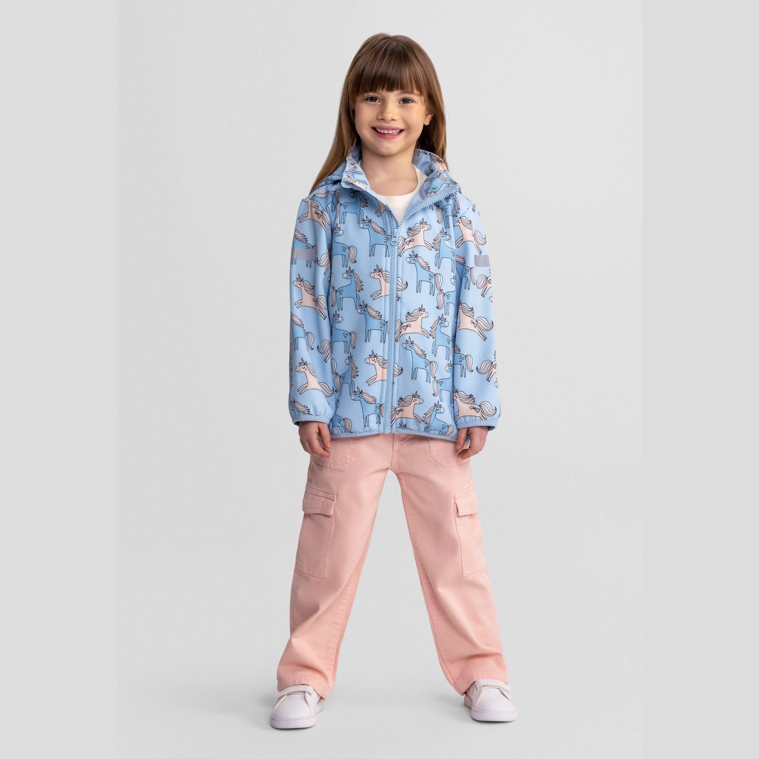 Young girl wearing light blue unicorn print softshell jacket with removable hood and pink cargo trousers, standing against white studio background