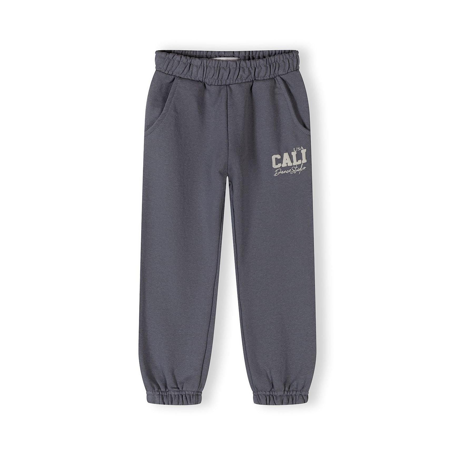 Close-up of blue-grey tracksuit bottoms showing elastic waistband and CALI USA Dance Studio text print on the leg