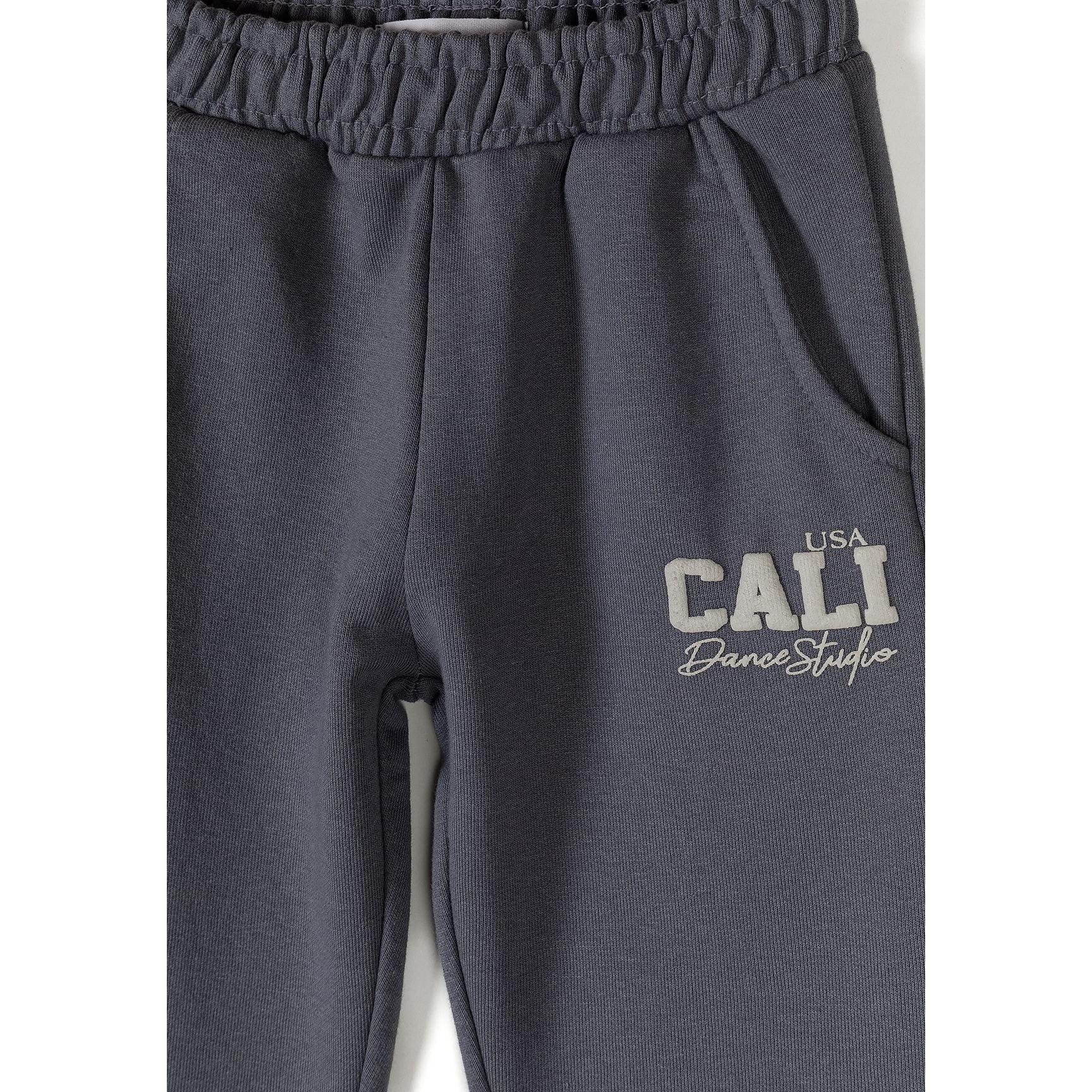 Close-up of blue-grey tracksuit bottoms showing elastic waistband and CALI USA Dance Studio text print on the leg