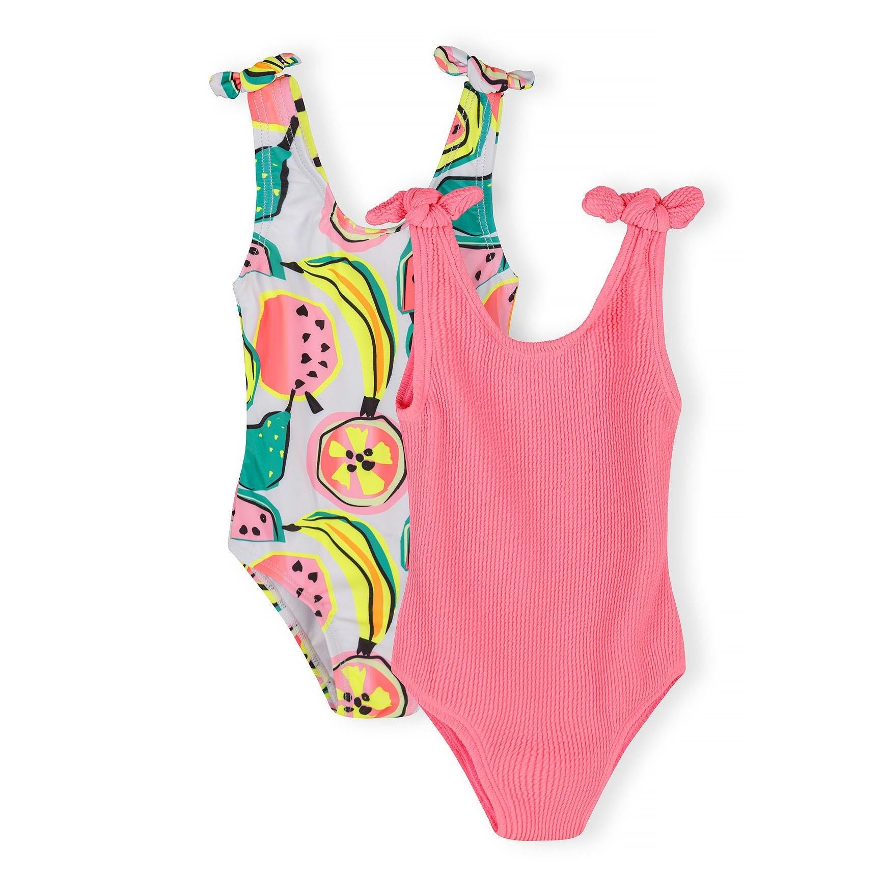 Two children's swimsuits laid flat on white background - one with colorful tropical fruit print featuring watermelons and bananas, one solid coral pink with ribbed texture and tie shoulder straps