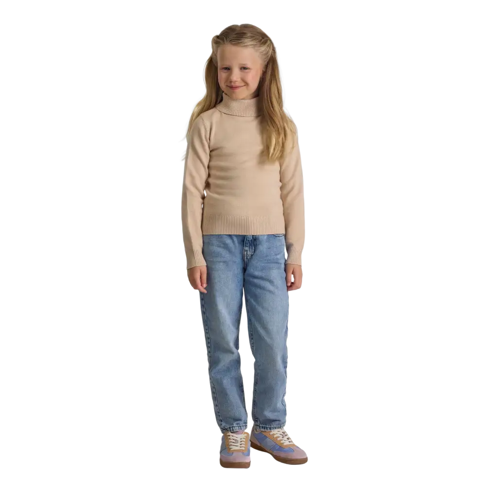 Young blonde girl wearing beige turtleneck jumper with blue jeans and sneakers, standing against black background, smiling at camera