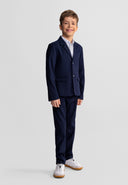 Young boy wearing a tailored navy blue blazer with notch lapel, paired with matching pants and white sneakers