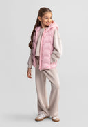 Girl wearing a lightweight pink nylon gilet with hood and zip, paired with beige casual outfit and sneakers, showcasing design.