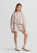 Young girl wearing a beige sweatshirt and shorts set with elasticated waist, showcasing a stylish, comfortable design.