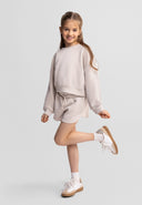 Smiling girl wearing beige sweatshirt and shorts set with elasticated waist, showcasing casual kids fashion design.