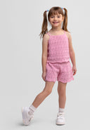 smiling young girl in pink crochet two-piece outfit standing on one leg with hands relaxed by sides