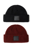 Two knitted fisherman hats in black and burgundy with front badge detail.