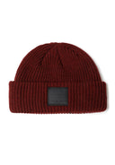 Detail of a knitted fisherman hat in dark red with a front badge.