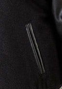 Detail of a boys baseball jacket showing black faux leather and felt fabric.