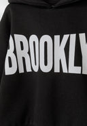 Close-up of a black girls' hooded tracksuit featuring a large white 'BROOKLYN' print.