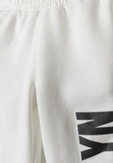 Detail of white joggers with elastic waistband and black print.