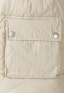 Detail of a cream padded gilet with snap fastening and a pocket.