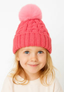 Close-up of a pink knitted cable hat for girls, featuring a pom pom on top.