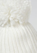 Detail of a cream knitted baby hat with a pom pom and ear pieces.
