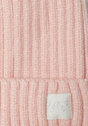 Detail of a pink ribbed baby beanie with a pom pom and a subtle logo badge.