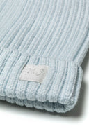 Detail of a blue ribbed beanie with a logo badge and pom pom, suitable for babies 0-24 months.