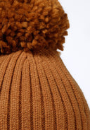 Close-up of a beige knitted baby hat with a pom pom and ear pieces.