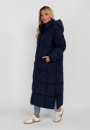 Women long quilted navy winter jacket with drawstring hood and zippers, side view.