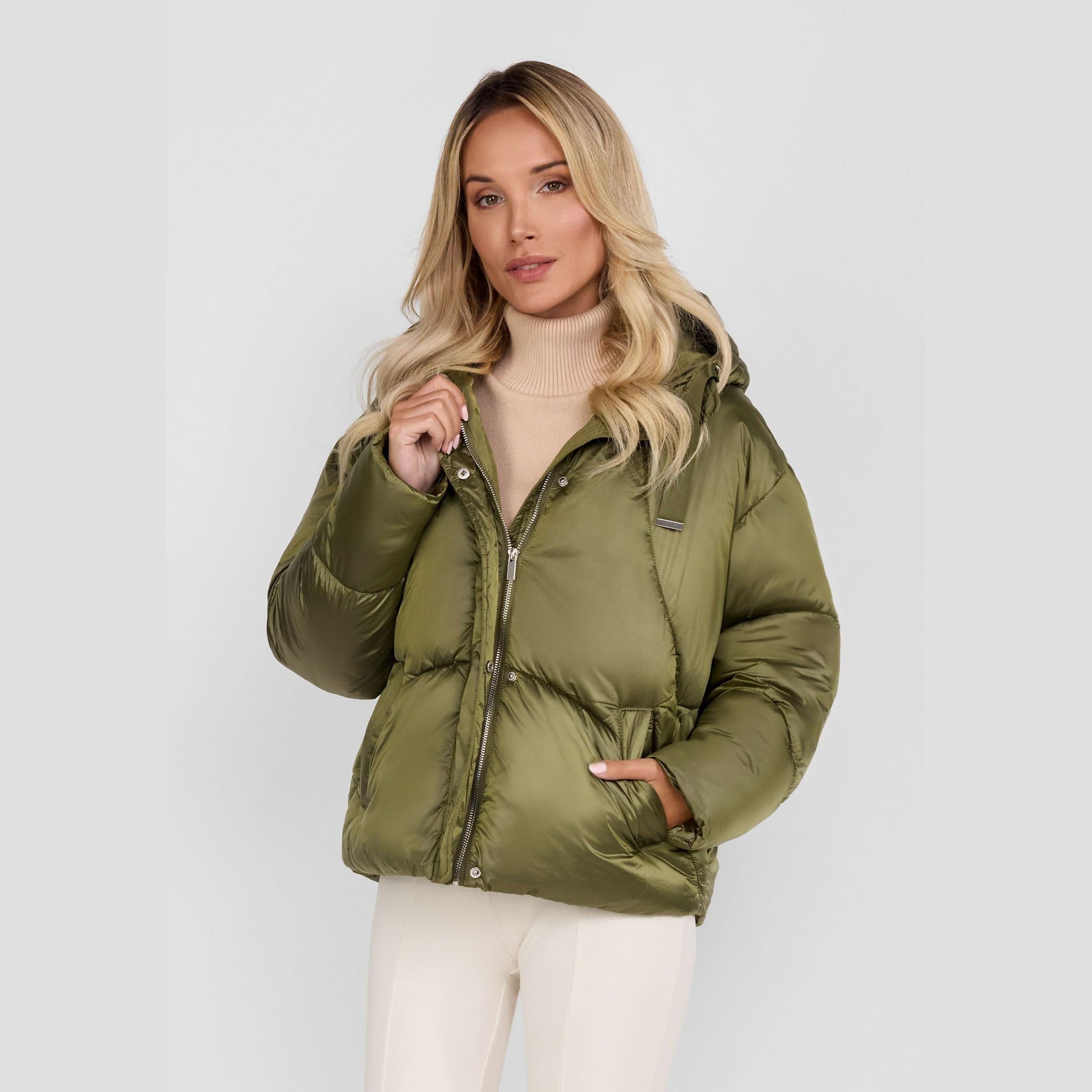 Woman wearing olive green quilted puffer jacket with hood and beige turtleneck sweater against white background