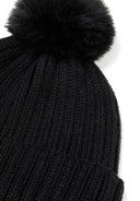 Close-up of a black knitted beanie hat with a faux fur pom pom and ribbed texture.
