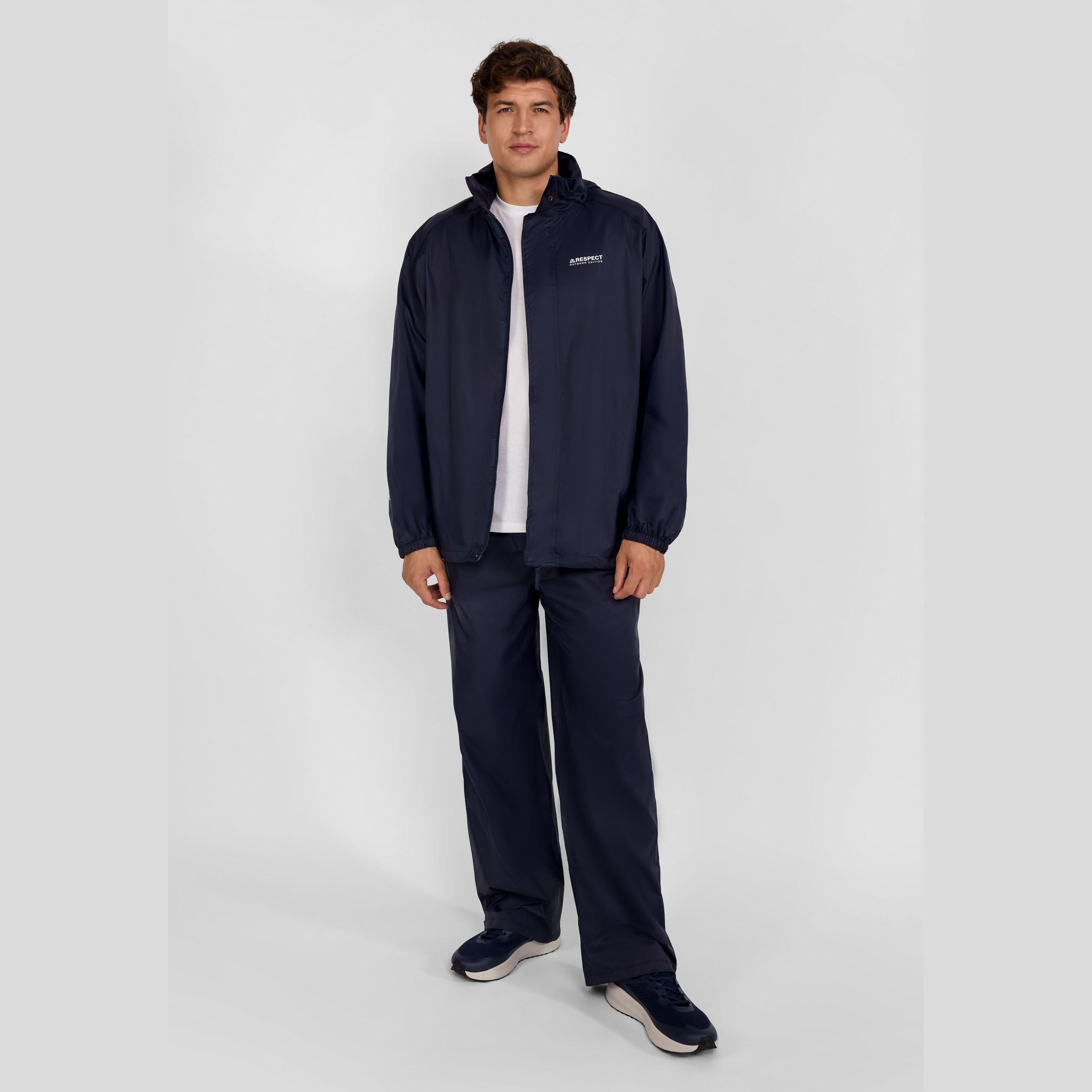 Young man wearing navy waterproof overpants with matching jacket and white t-shirt, standing against white background in full length view