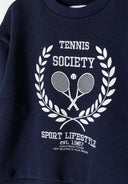 Detail of a girls navy fleece crew neck sweatshirt featuring a tennis-themed print.