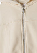 Detail of a beige cropped zip hoodie featuring a full-length zipper and attached hood.