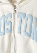 Detail of a cream cropped zip-through hoodie featuring a blue printed design and a silver zipper.