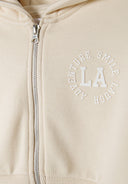 Detail of a beige zip-through hoody featuring a front print and ribbed cuffs.