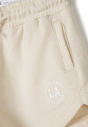 Detail of beige shorts with pockets and front print.