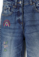 Detail of girls' straight leg jeans in navy with embroidered rainbow and floral accents.