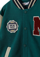 Close-up of boys green fleece baseball jacket, featuring decorative patch and button details.