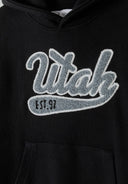 Close-up of a black boys oversized hoodie featuring a kangaroo pocket and decorative Utah print.