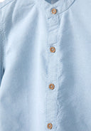 Detail of a grandad-style shirt with button fastening in light blue.