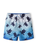 Boys board shorts in light blue with turtle print, front view, featuring drawstring and side pockets.