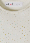 Close-up of cream baby bodysuit with colorful small polka dot design and MINOTI label inside collar.