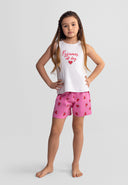 Young girl wearing white ribbed tank top with pink 'Pyjamas all day' text and heart design, paired with pink watermelon print shorts, standing against light background