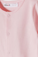 Close-up of soft pastel pink sleepsuit with snap button closure and MINOTI label for baby girls.