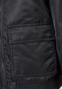 Detail of a black nylon bomber jacket showing utility pocket and zipper.