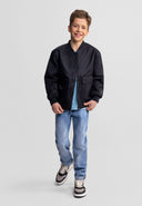 Smiling boy wearing a black nylon bomber jacket with utility pockets and casual jeans on a light background