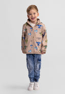 Young boy smiling wearing a softshell jacket with colorful aeroplane design and casual jeans standing against white background