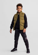 Smiling boy wearing olive padded nylon utility waistcoat with stand collar and flap pockets in casual kids fashion style