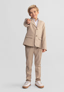 Boy wearing stone color formal suit trousers with adjustable waistband, smiling confidently and pointing forward with stylish design.