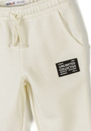 Close-up of cream-colored boys tracksuit bottoms with elastic waist and branded patch detail on thigh panel.